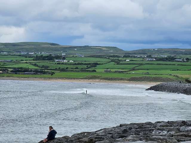 Longboard surfer riding a knee high wave at the north end of the beach with the tide on the rocks